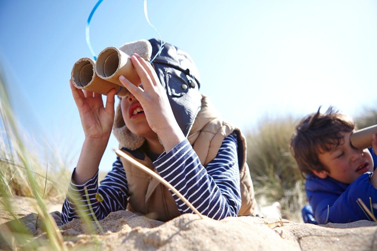 young boy using handmade binoculars in the sand looking for birds
