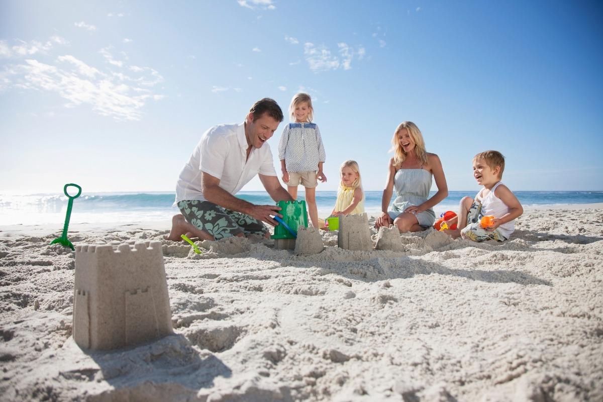 family playing together in the sand builind a sandcastle on the beach