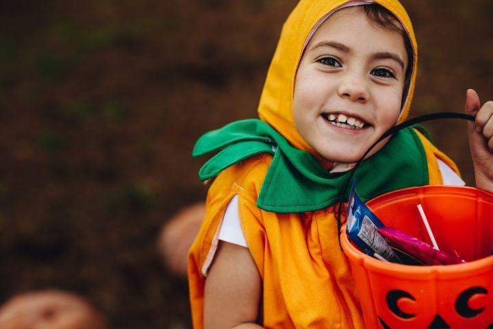 close up portrait of cute little girl holding a pumpkin bucket in halloween costume outdoors at park.