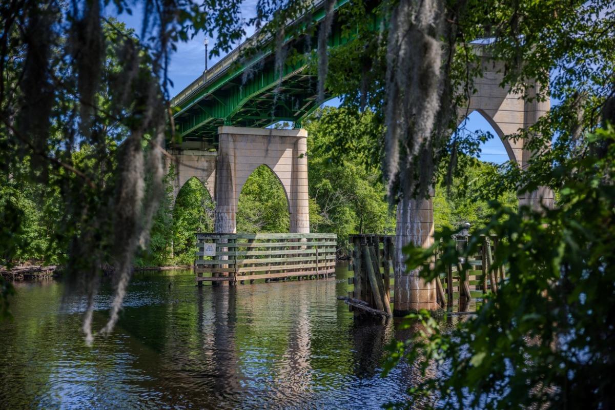 A serene view from the Conway Riverwalk of Waccamaw River and Waccamaw River Memorial Bridge at Conway, South Carolina, with out-of-focus live oak tree and Spanish moss in the foreground